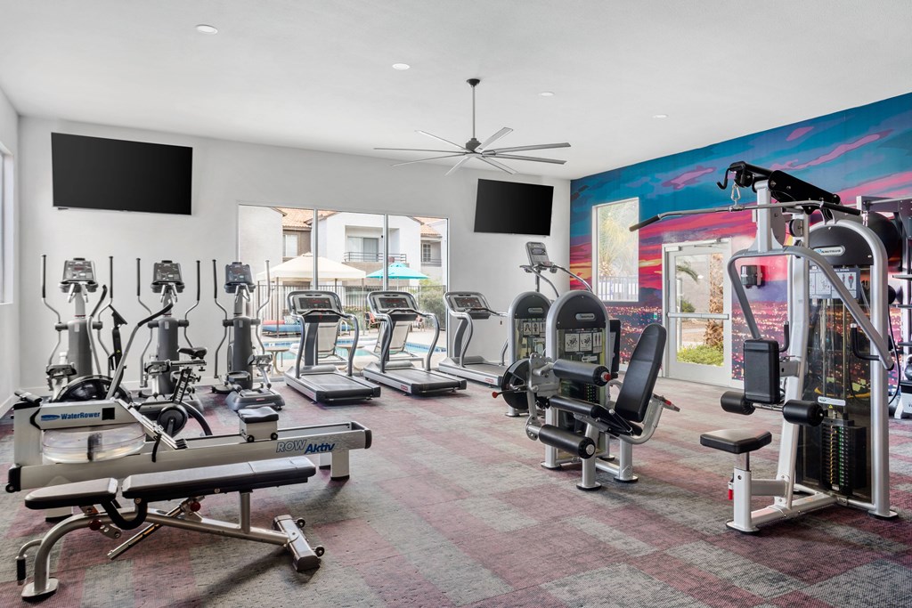 a spacious fitness room with cardio equipment and flat screen televisions